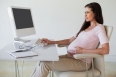 Casual pregnant businesswoman touching her bump at her desk in her office