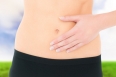Closeup mid section of a fit woman with stomach pain against tree in green field