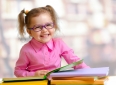 Happy child girl in eyeglasses reading books sitting at table