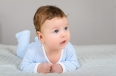 Cute smiling baby boy in bed lying on his belly in bedroom