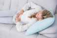 Blonde lying on couch getting stomach pain at home in the living room