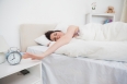 Sleepy woman in bed extending hand to alarm clock