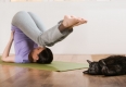 Woman in a traditional stretching yoga pose at home with her cat