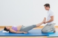 Masseur lifting pregnant womans legs on blue mat in a fitness studio
