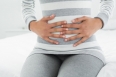 Close-up mid section of a casual young woman with stomach pain sitting in bed at home