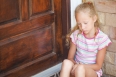 sad little girl sitting near a door on the background of an bric