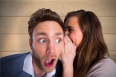 Woman whispering secret into friends ear against bleached wooden planks background